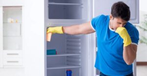 Man cleaning smelly refrigerator wearing yellow gloves.