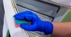 Hand wearing blue glove cleaning refrigerator seal with sponge.
