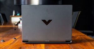 Dark grey gaming laptop (Victus) on a wooden conference table.
