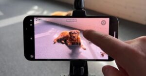 Hand tapping on a smartphone screen recording a brown dog lying on the ground.