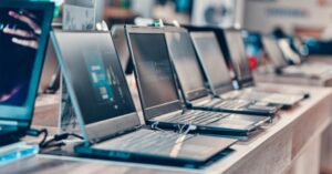 Row of display laptops for sale in an electronics store on a wooden shelf.