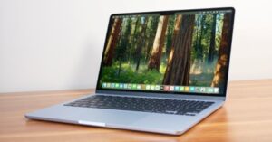 MacBook Pro displaying a beautiful forest wallpaper on a wooden desk.