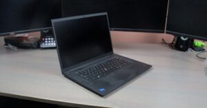 Black professional laptop on a wooden desk with multiple external monitors.