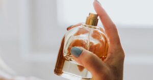 Close-up of a hand holding a golden glass perfume bottle.