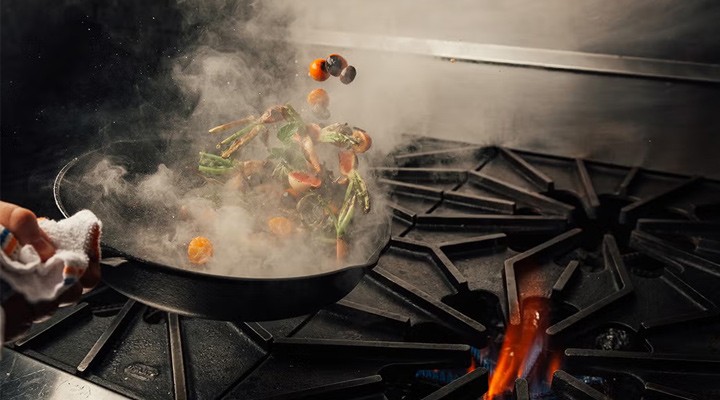 Close-up of stir-frying technique with vegetables flying out of a skillet.