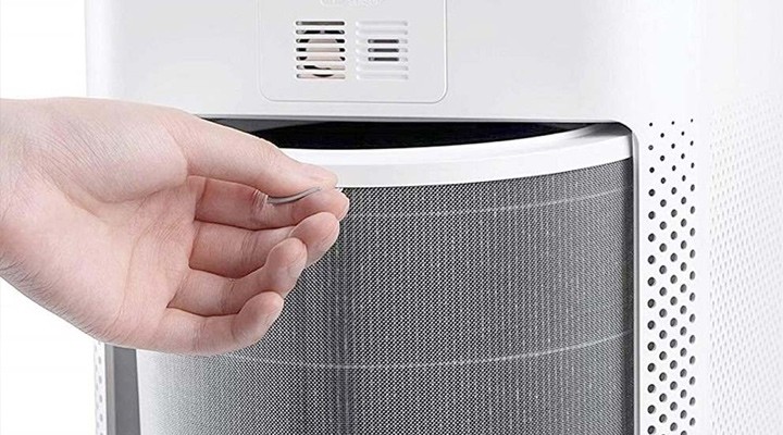 Hand replacing or checking the circular filter inside a white air purifier.
