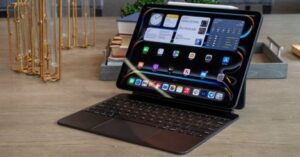 iPad Pro on Magic Keyboard showing Home Screen with widgets and dark mode.
