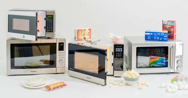 Three microwave ovens with open doors, popcorn, and packaged microwave food products for kitchen appliance comparison