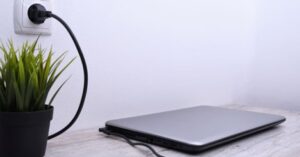 Laptop connected to wall charger on desk next to plant 