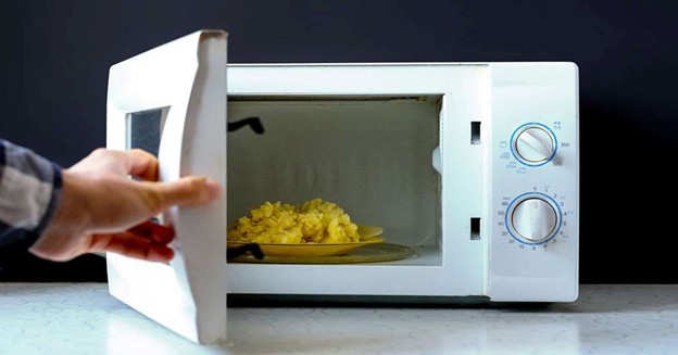 Hand opening a microwave oven with heated food inside for safe kitchen appliance use