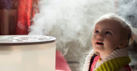 Child sitting near a humidifier producing mist indoors