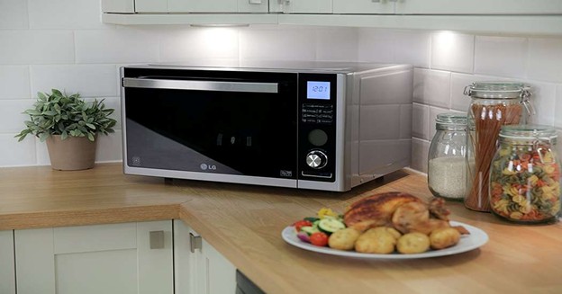 LG microwave oven on kitchen countertop with roasted chicken, potatoes, pasta jars, and modern cabinets