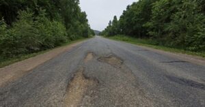 damaged road with potholes causing tire wear and suspension damage on rough driving conditions
