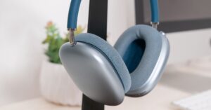 AirPods Max headphones with blue ear cushions displayed on a desk stand