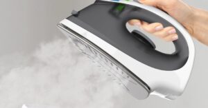 Steam iron releasing strong steam from the soleplate during clothes ironing.