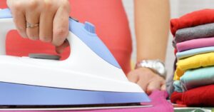Ironing colorful clothes with a steam iron beside folded laundry.