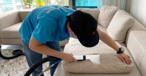 Professional cleaning a beige fabric sofa with upholstery extraction equipment.