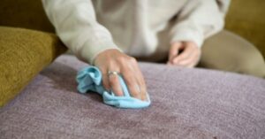 Wiping stains from fabric upholstery with a blue cleaning cloth.