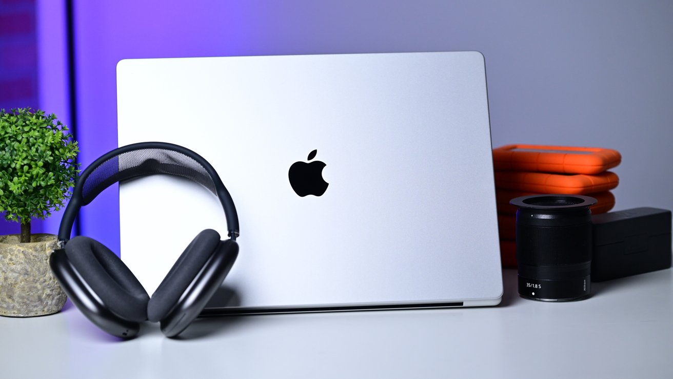 Apple MacBook on a desk with headphones, camera lens, and digital accessories
