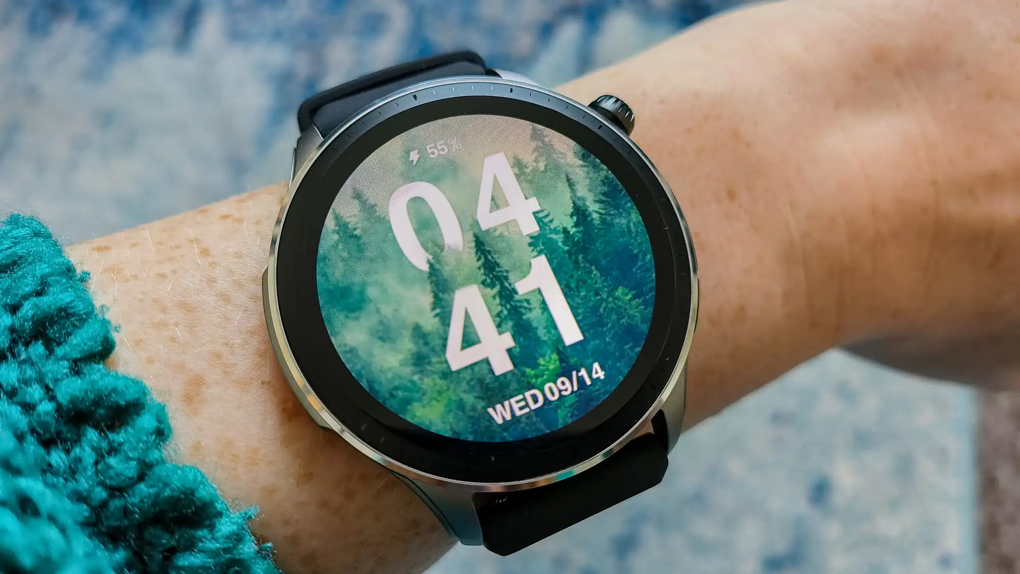 Round smartwatch on a wrist with forest-themed digital display and black strap 