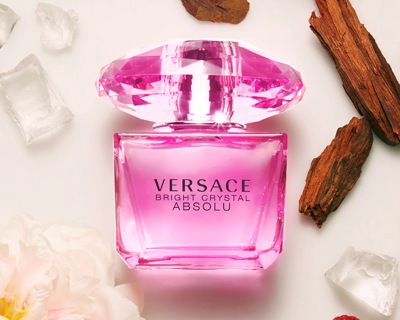 Pink Versace Bright Crystal Absolu perfume bottle with flowers, ice cubes, and wood pieces

