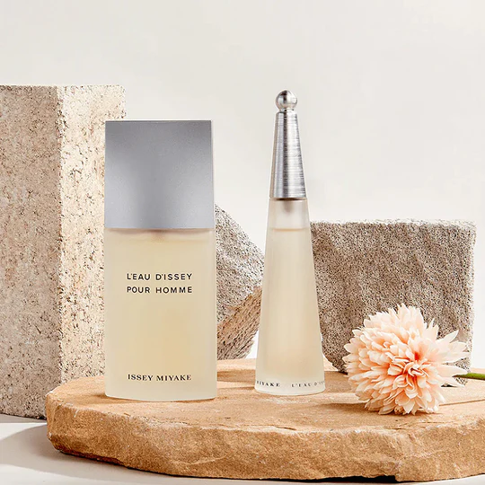 Issey Miyake L’Eau d’Issey perfume bottles displayed with a flower on a neutral stone background
