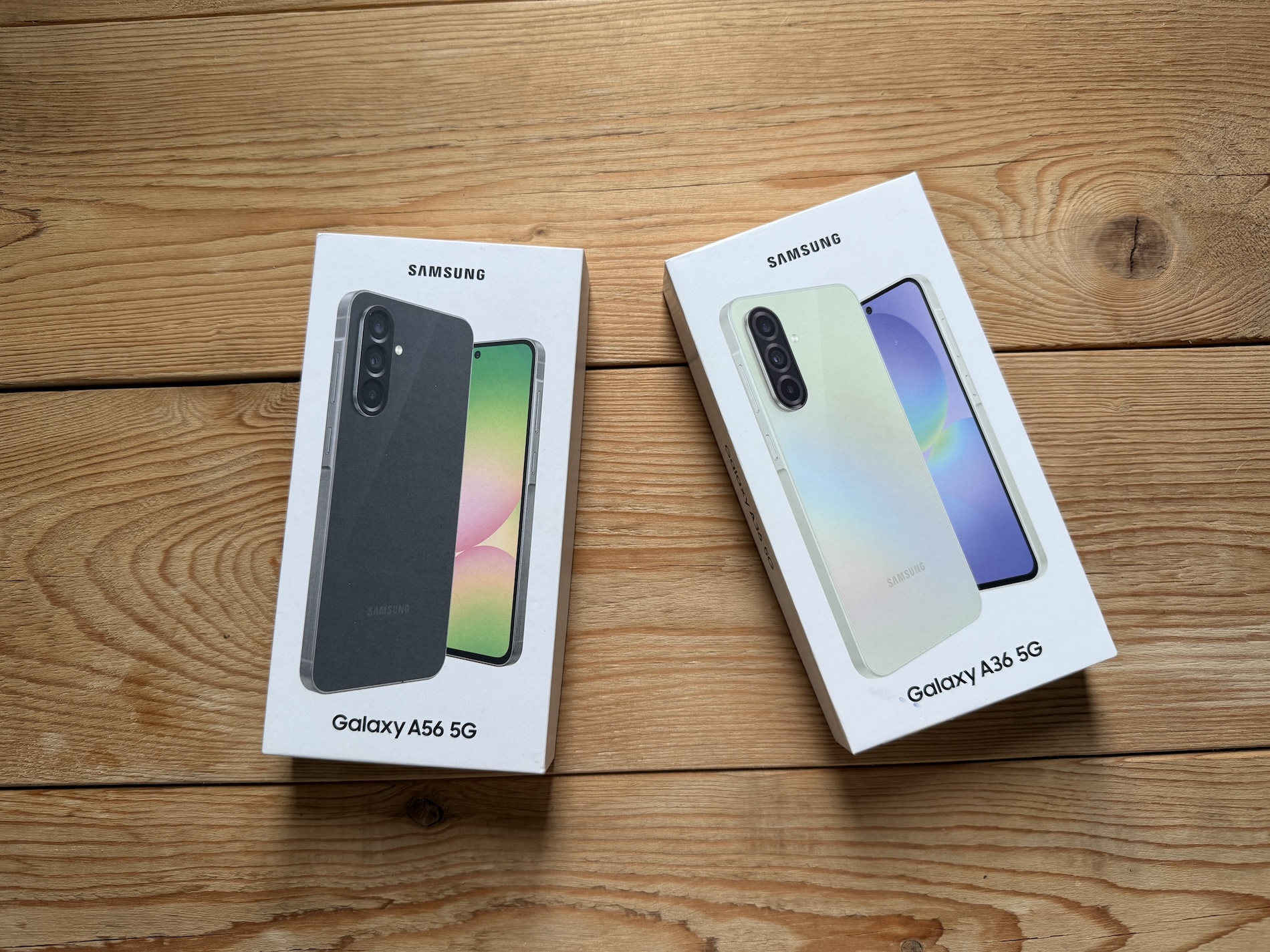 Samsung Galaxy A56 5G and Galaxy A36 5G retail boxes displayed side by side on a wooden surface. 