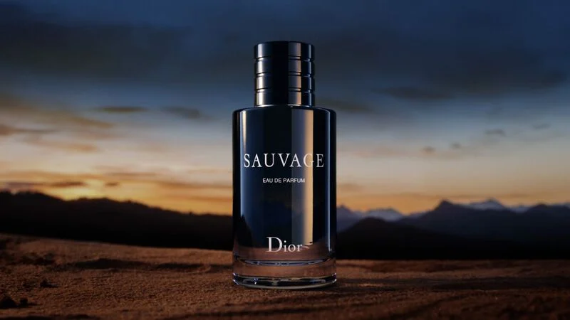 Dior Sauvage Eau de Parfum bottle against a dramatic sunset landscape background. 