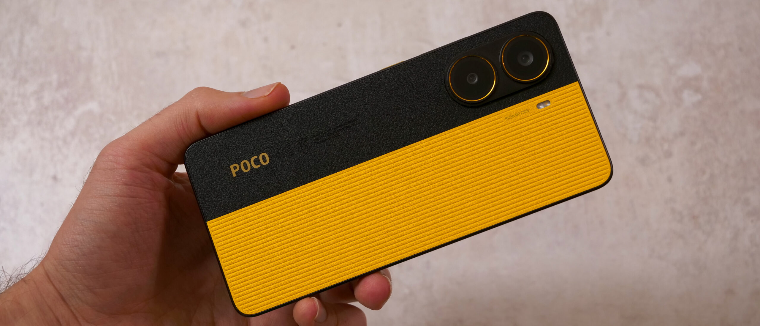 POCO smartphone in black and yellow finish held in hand, featuring a dual-camera system, textured back panel, and distinctive gaming-inspired design.