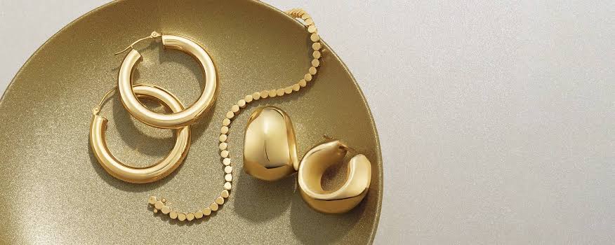 Gold hoop earrings, chain bracelet, and statement rings arranged on a gold tray.