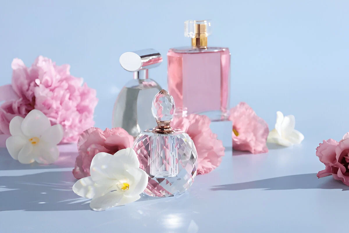 Perfume bottles surrounded by pink and white flowers on a soft blue background