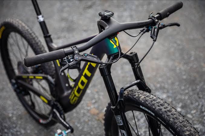 Mountain bike handlebars, brake levers, suspension fork, and front tire shown in close-up.