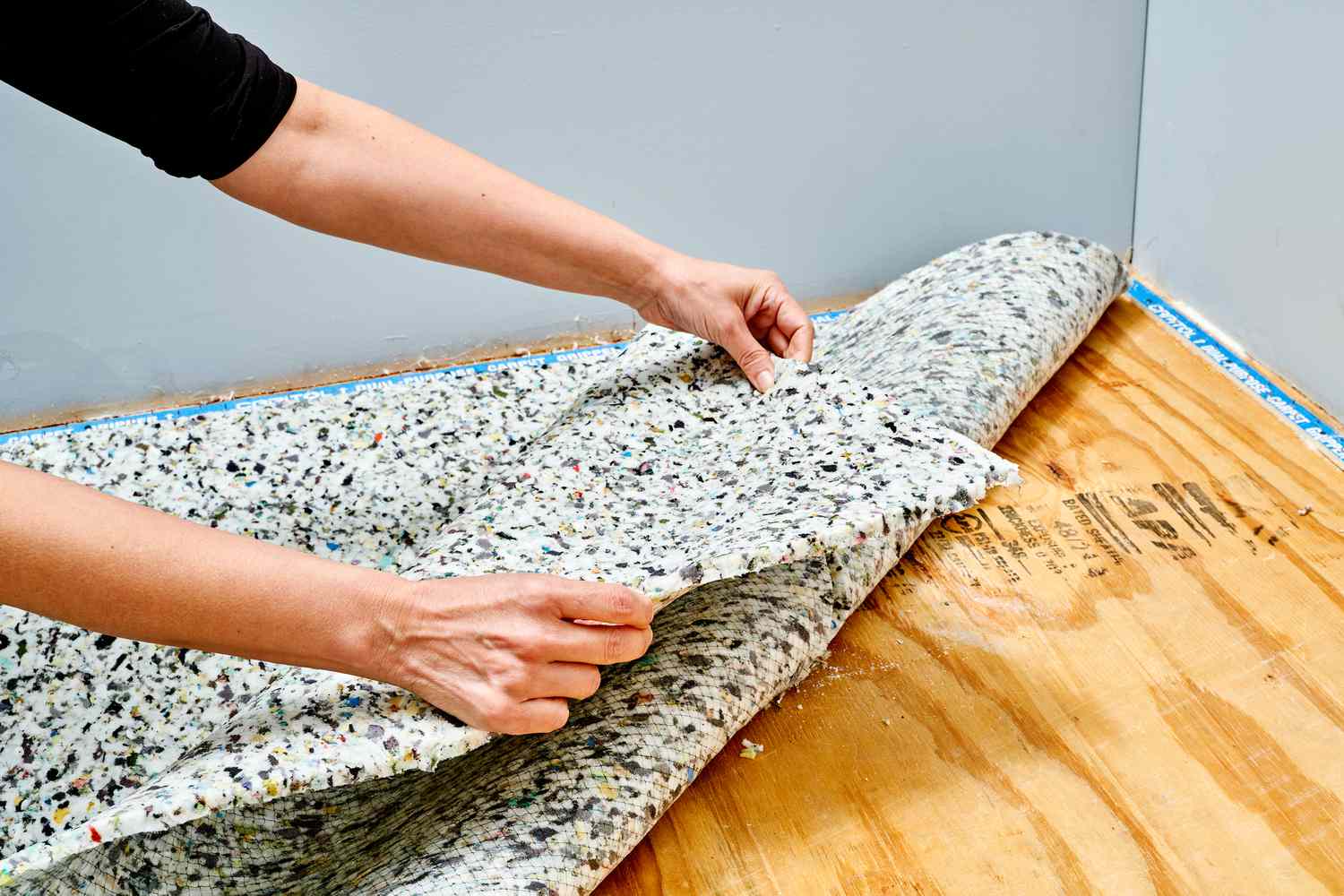Person installing carpet padding under a rug on a wooden floor.