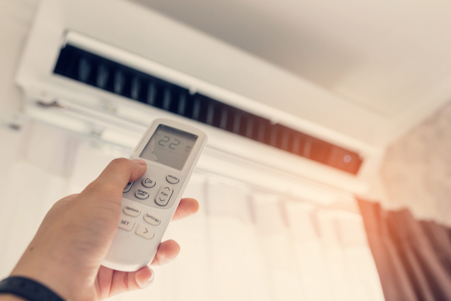 Hand using a remote control to adjust a wall-mounted air conditioner set to 22°C
