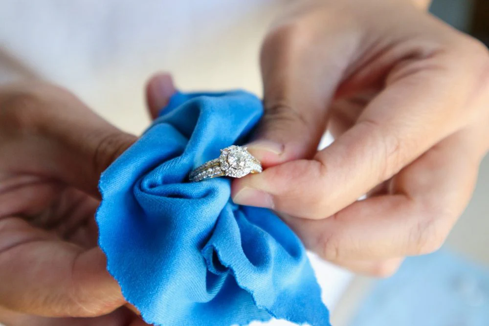 Person polishing a diamond ring with a soft blue cloth.
