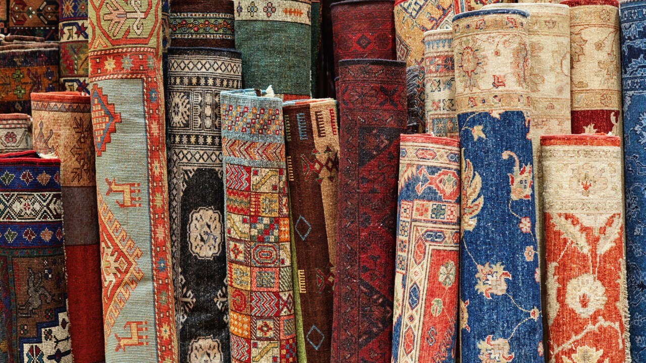 Colorful Persian rugs rolled and displayed together in a carpet market.