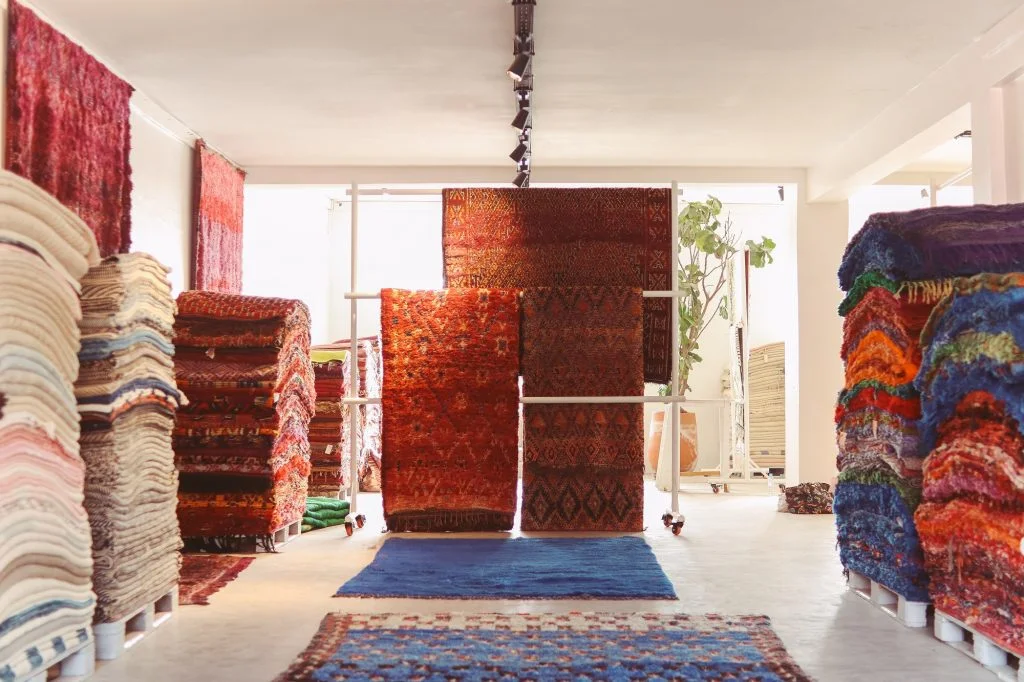 Carpet shop interior with colorful Persian rugs displayed on shelves and racks.