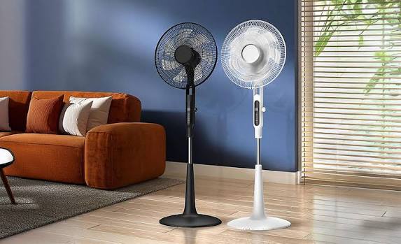 Two standing fans positioned beside a sofa and window in a modern living room
