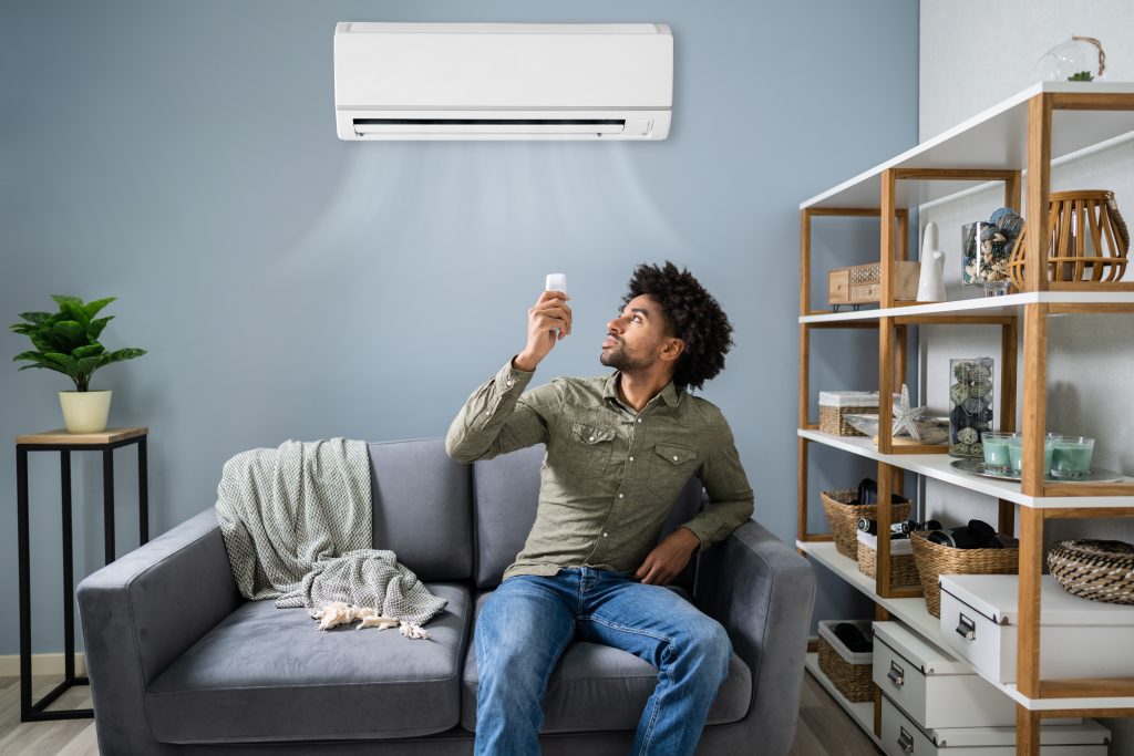 Person using a remote control to adjust a wall-mounted air conditioner in a living room 