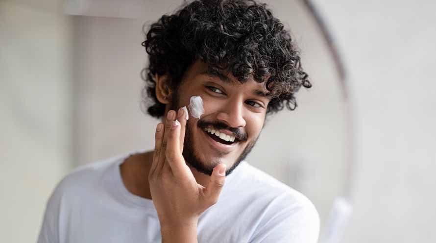 Man applying sunscreen cream to his face in front of a mirror