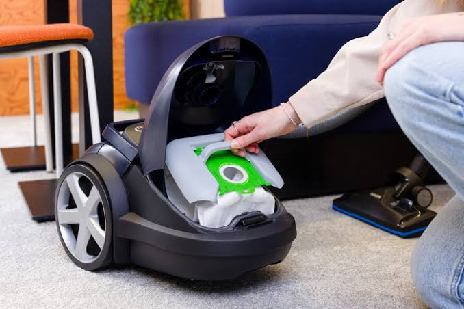 Person replacing a vacuum cleaner dust bag inside an open canister vacuum
