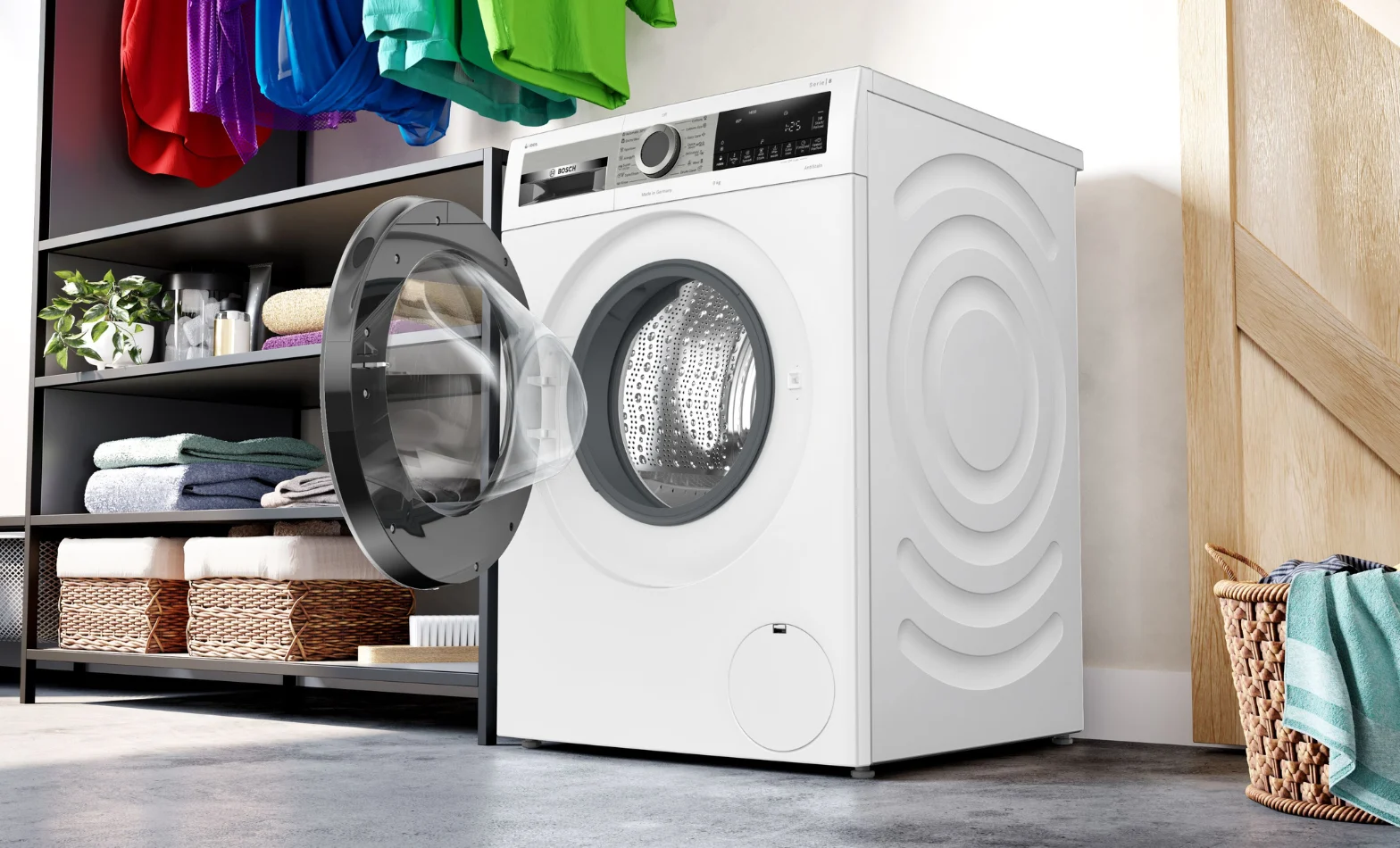 Open front-loading washing machine in a modern laundry room with folded towels and baskets