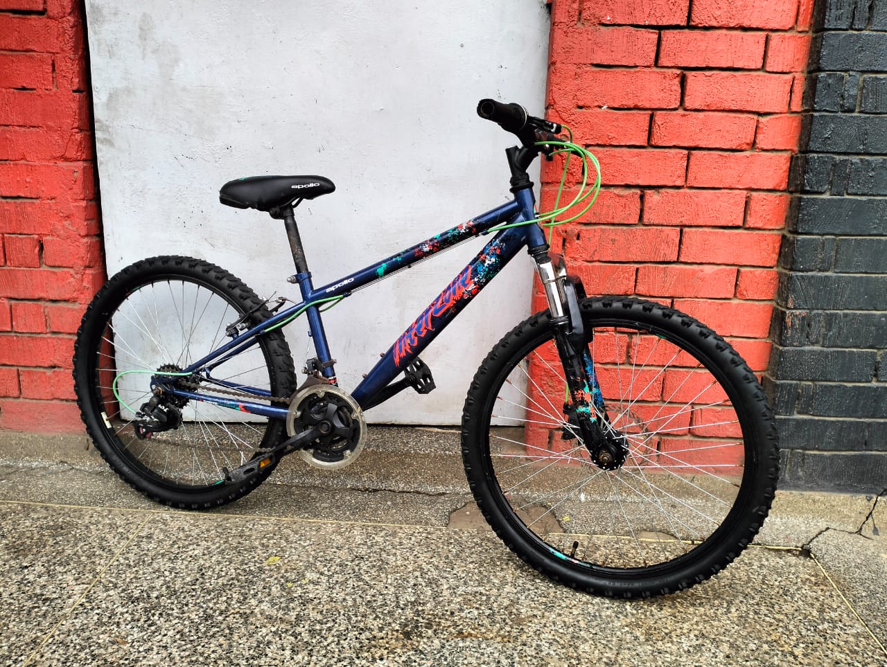 Mountain bike with front suspension and thick tires parked against a red brick wall.