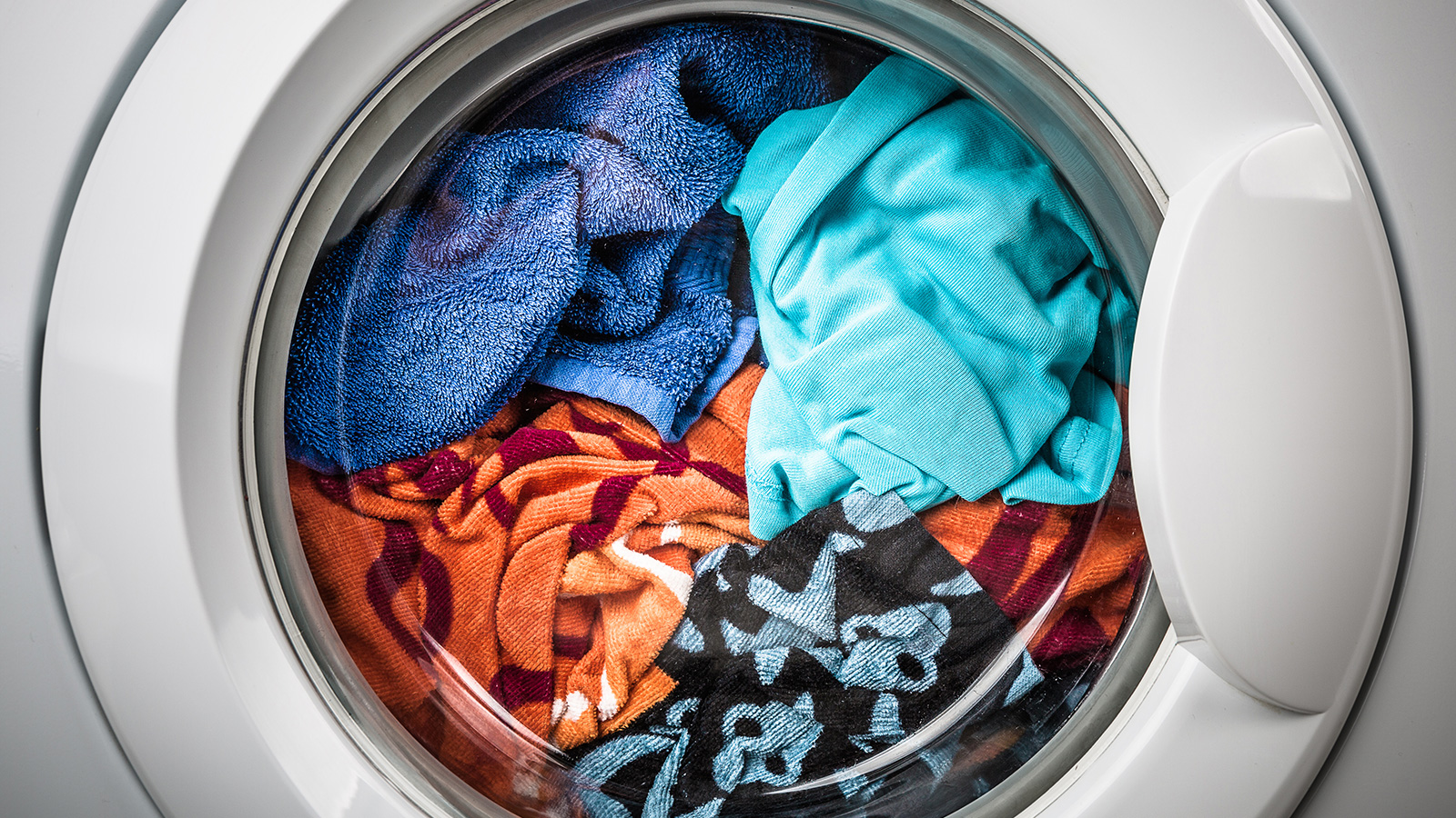 Front-loading washing machine filled with colorful clothes and towels