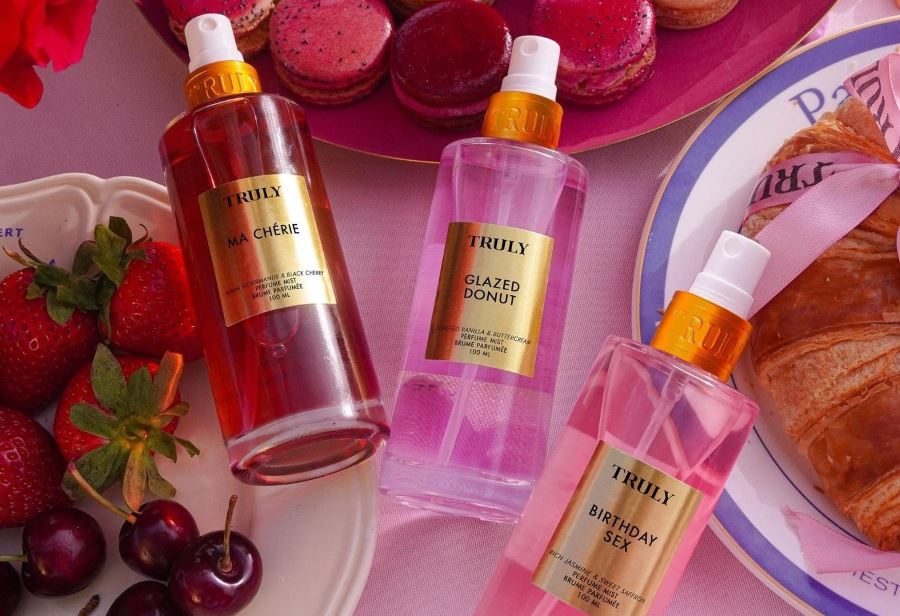 Colorful body mist bottles arranged with strawberries, cherries, desserts, and pink aesthetic decor