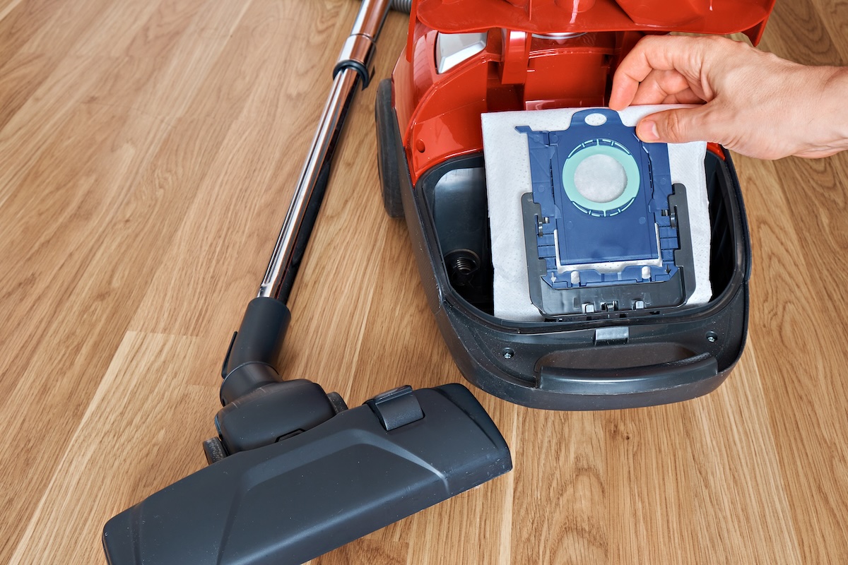 Person replacing a dust bag inside an open canister vacuum cleaner
