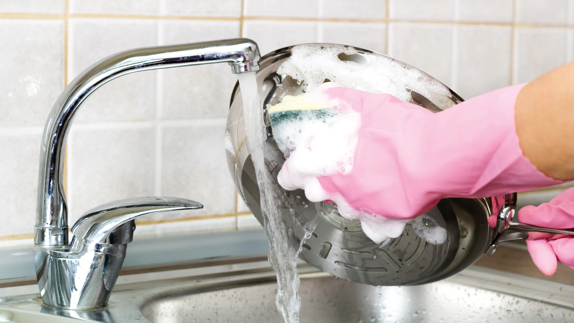 Person washing cookware with soapy water under a running kitchen faucet.