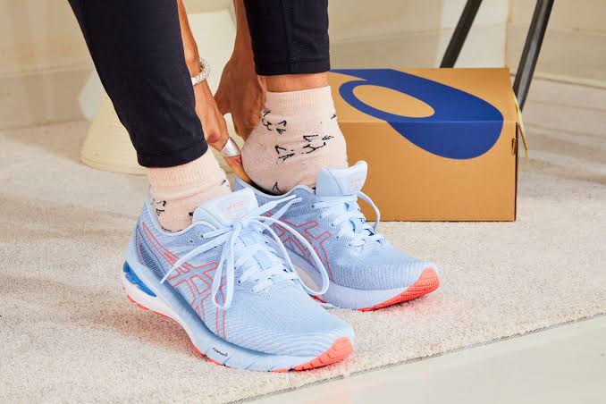 Person wearing light blue running shoes with shoebox in the background.
