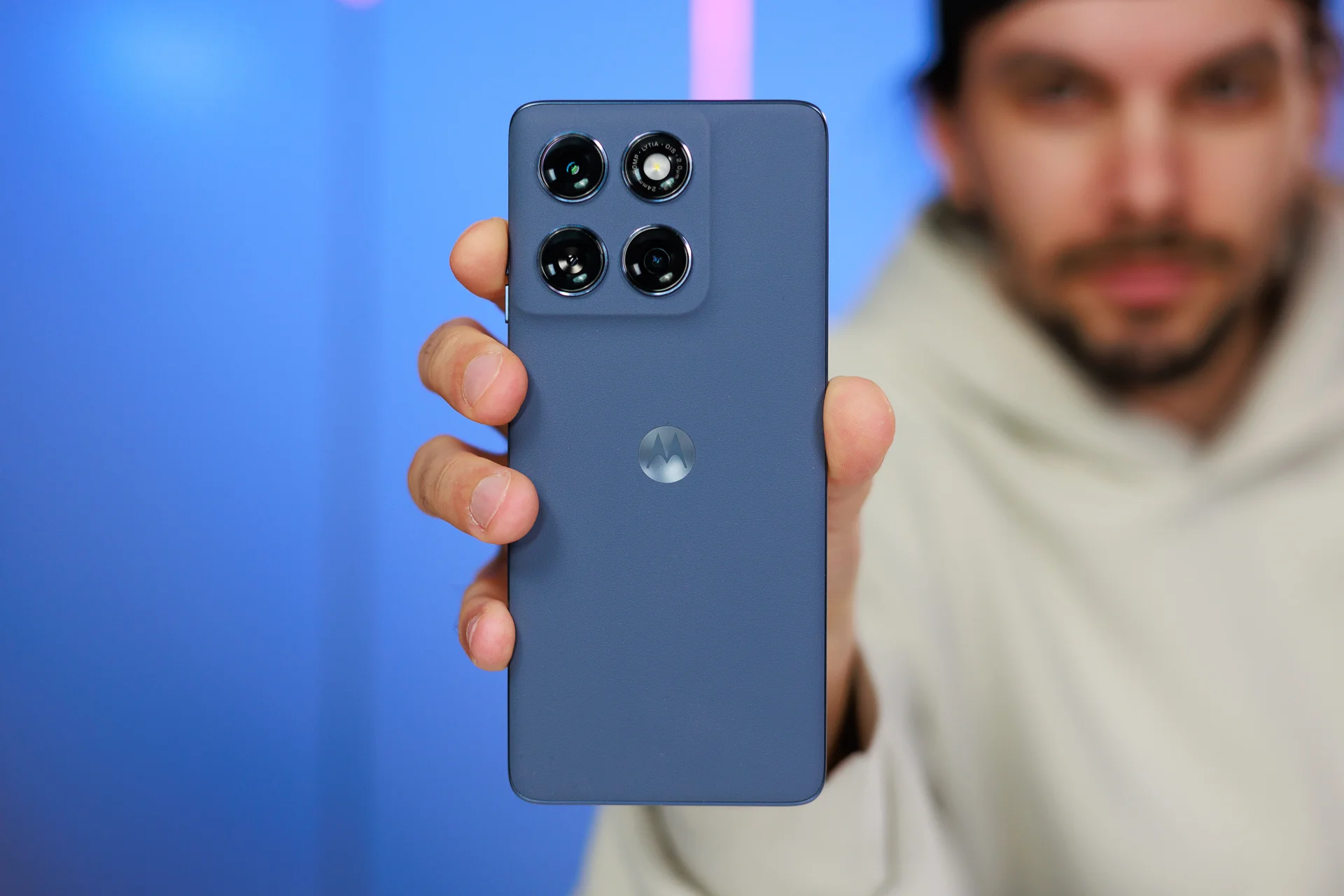 Man holding a blue Motorola smartphone close to the camera against a blurred background.
