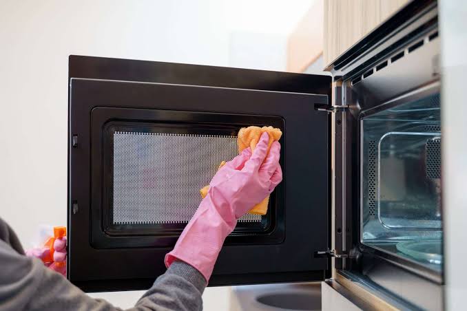 Person cleaning the inside of a microwave door with a soft cloth.
